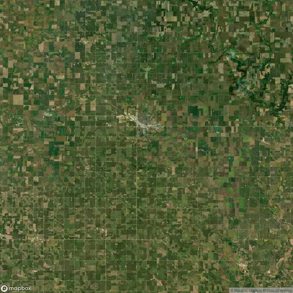 Aerial view of a vast, patchwork-like rural landscape with fields and scattered small town in the center, showing a grid pattern of agricultural plots and roads.