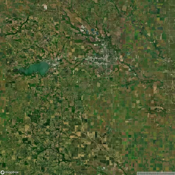 Aerial view of a large patchwork of agricultural fields and a visible town, with a lake in the upper left quadrant, showcasing rural landscape and infrastructure.