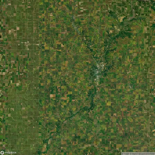 A satellite view of a patchwork agricultural landscape with fields and varying shades of green and brown. A river meanders vertically through the center of the image.