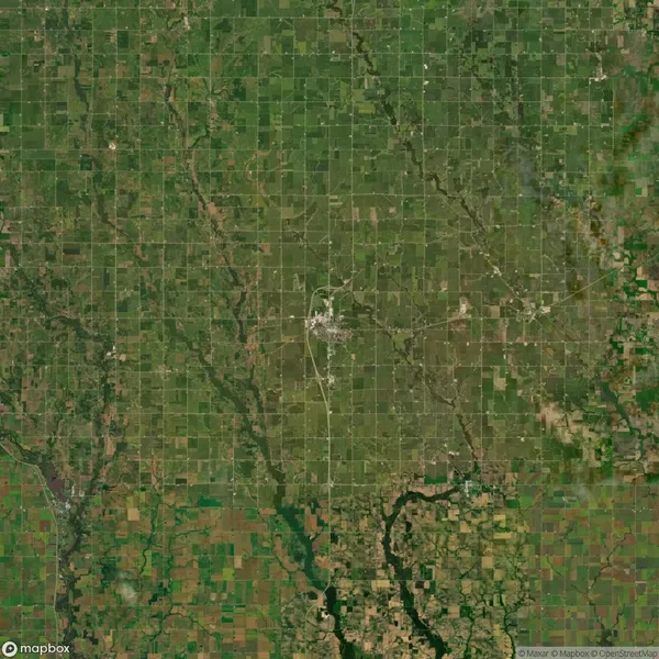 Aerial view of a rural landscape with a small town in the center, surrounded by a grid of agricultural fields and intersecting roads.