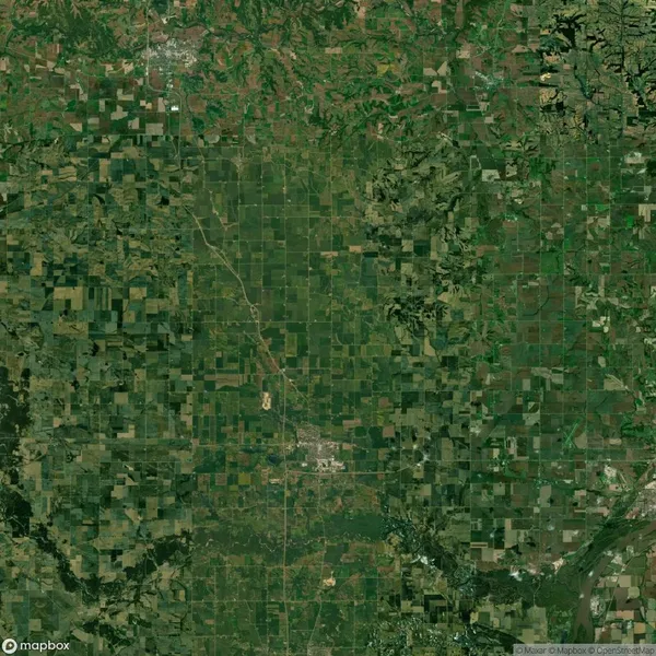 Aerial view of a large patchwork of agricultural fields and natural areas, showcasing a mix of greens and browns with a river at the bottom right corner.