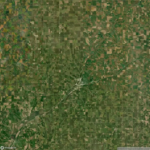 An aerial view of a rural landscape featuring a patchwork of green and brown fields with a small town and roads in the center.