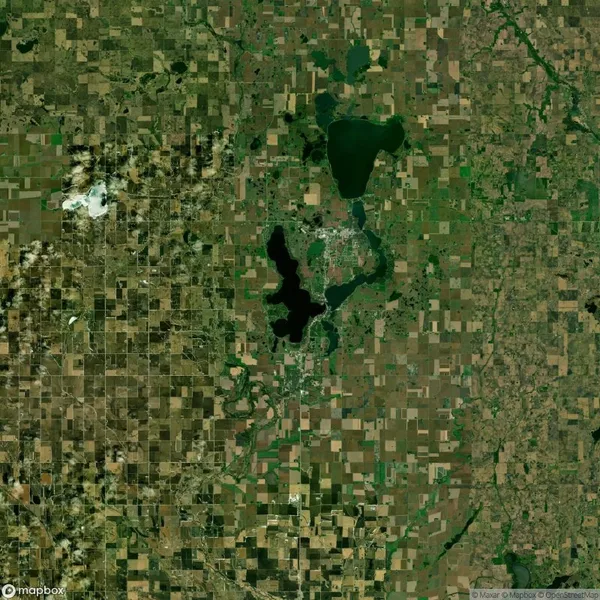 Satellite view of a landscape with a mix of green fields and brown patches, featuring two irregularly shaped lakes in the center.