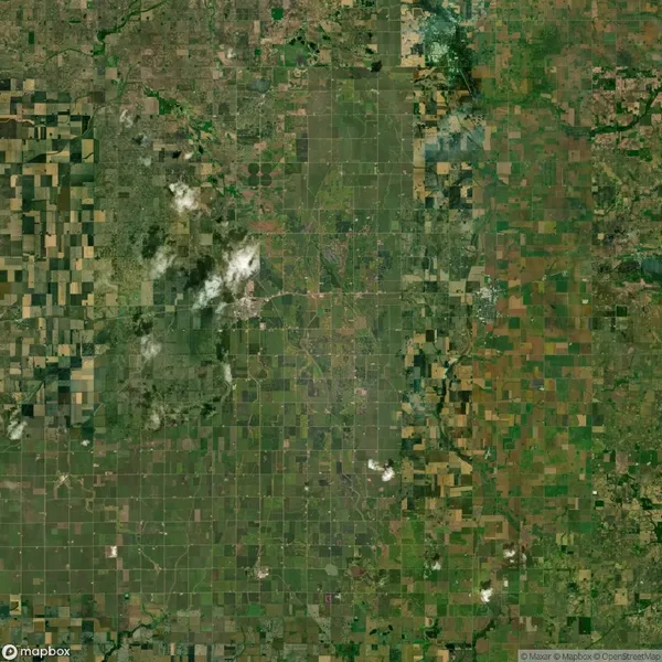 Aerial view of a large, flat agricultural landscape with green and brown patchwork fields and scattered clouds in the sky.