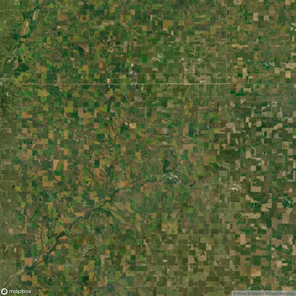 Aerial view of a vast patchwork of agricultural fields with varied shades of green and brown, interspersed with roads and a small river winding through the landscape.