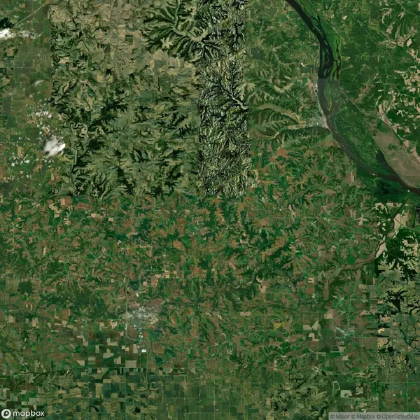 Aerial view shows a green, grid-like agricultural landscape with a river on the right and varying terrain features in the upper section.