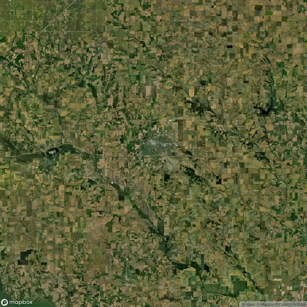 Aerial view of a rural landscape with patchwork fields, roads, and a small town center. Sparse vegetation is visible, suggesting a dry climate.