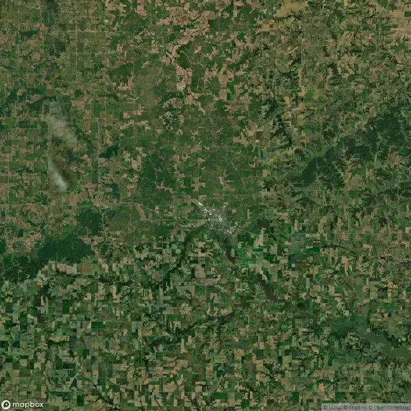 Satellite view of a rural landscape with a small town center surrounded by patchwork farmland, roads, and scattered woodland areas.