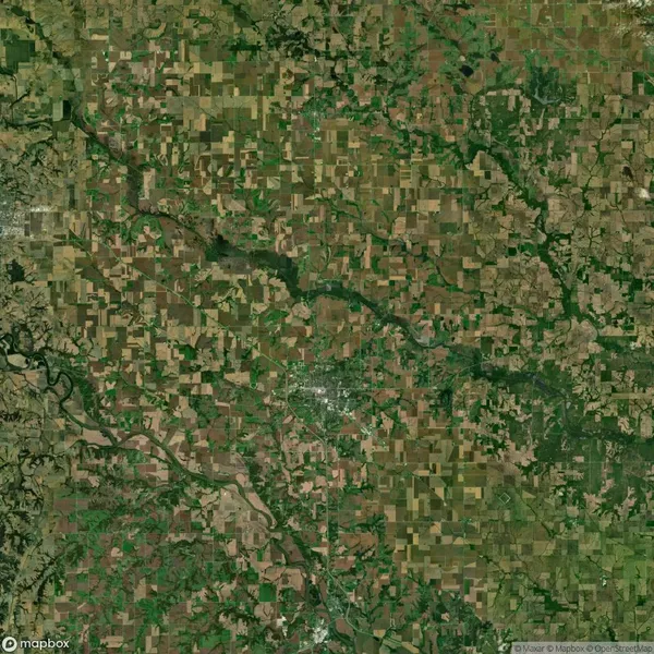 Aerial view of a rural landscape with a patchwork of agricultural fields, a river flowing through, and patches of forested areas.