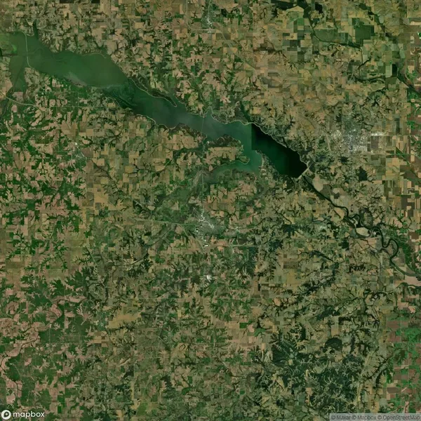 Satellite view of a green landscape with a winding river and a mix of agricultural fields and forests. A town is visible near the top right, and a large body of water extends across the image.