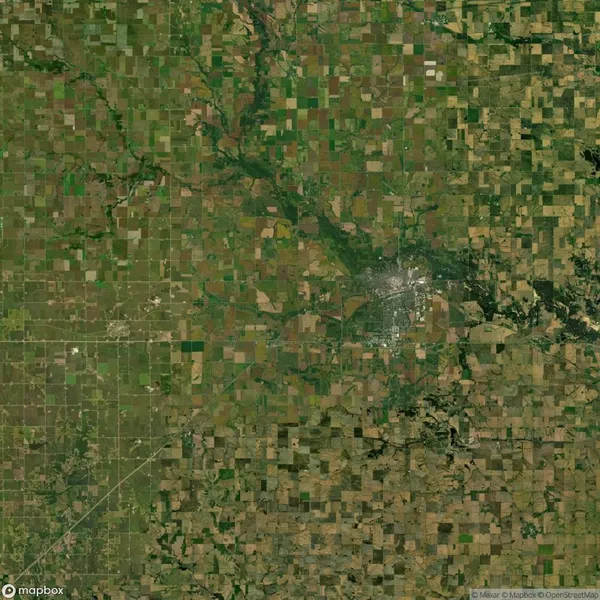 Aerial view of a large grid-like pattern of agricultural fields surrounded by greenery, with a town visible in the right center.