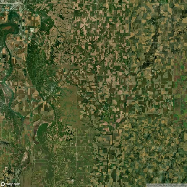 Aerial view of a patchwork of agricultural fields and green areas, surrounded by a river on the left. Roads and small settlements are visible across the landscape.