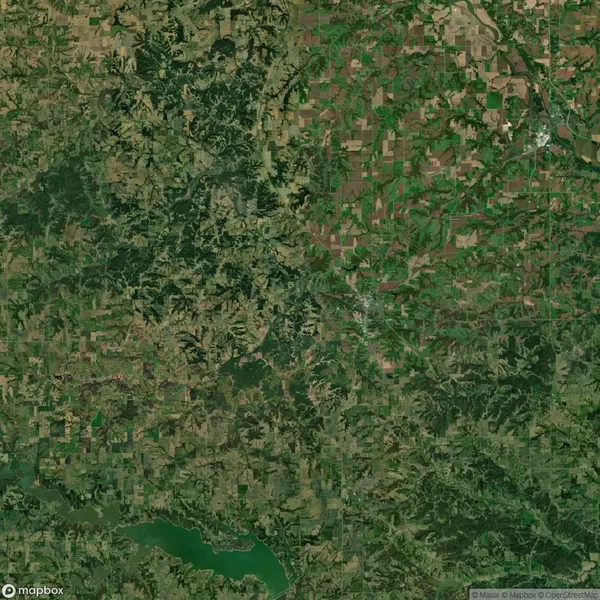 Aerial view of a rural landscape with a patchwork of fields, forests, and a winding river. A reservoir can be seen at the bottom left corner.