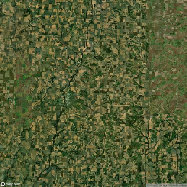 Aerial view of a patchwork landscape of fields and farmland, featuring various shades of green and brown, with a few winding roads and clusters of trees throughout.