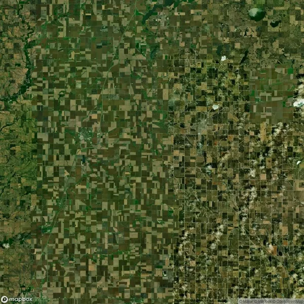 Aerial view of farmland with a grid-like pattern of fields and patches of green and brown, showing varied vegetation and land use.