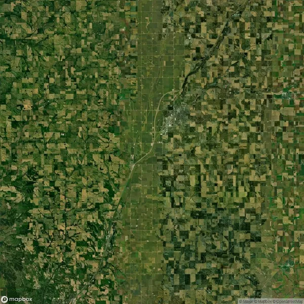 Satellite view of a landscape showing a patchwork of agricultural fields with a river winding through the center, dividing denser greenery on the left and sparser greenery on the right.