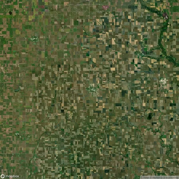 Aerial view of a large patchwork of agricultural fields, mostly rectangular and green, with some brown areas, intersected by a few winding roads and waterways.