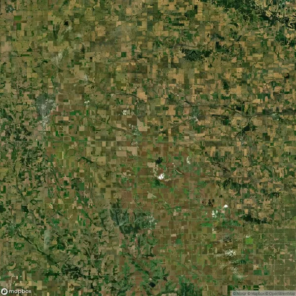 Satellite image showing a patchwork of agricultural fields and vegetation in varying shades of green and brown, intersected by roads and water bodies.