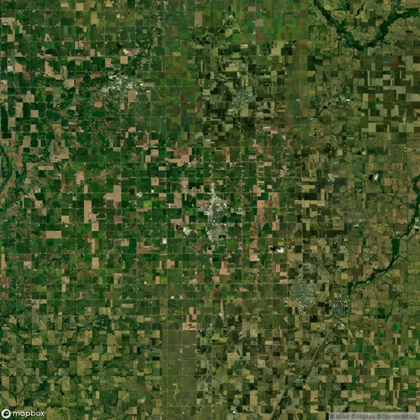 Aerial view of a rural landscape showing a patchwork of agricultural fields in varying shades of green and brown. Sparse clusters of buildings are visible throughout.