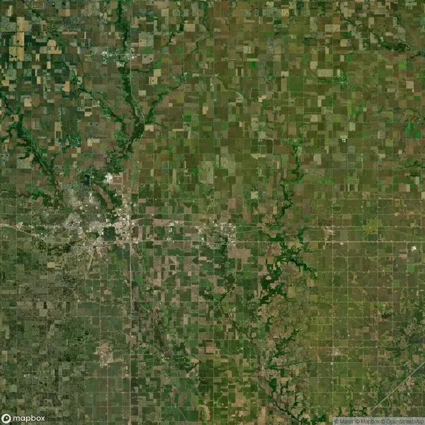Aerial view of a landscape featuring a patchwork of agricultural fields and a small town with surrounding greenery and roads.