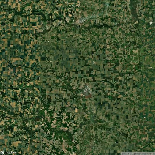 Aerial view of a landscape with a patchwork of agricultural fields in various shades of green and brown, interspersed with roads and small wooded areas.