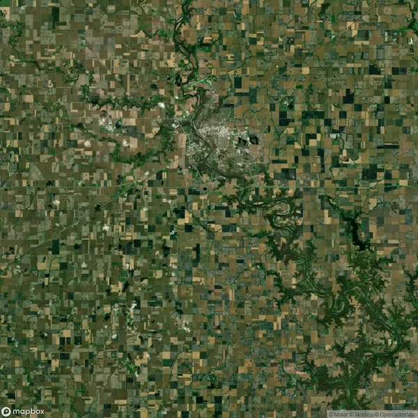Satellite image showing a patchwork of agricultural fields, roads, and a river winding through the landscape. A small urban area is visible near the center.