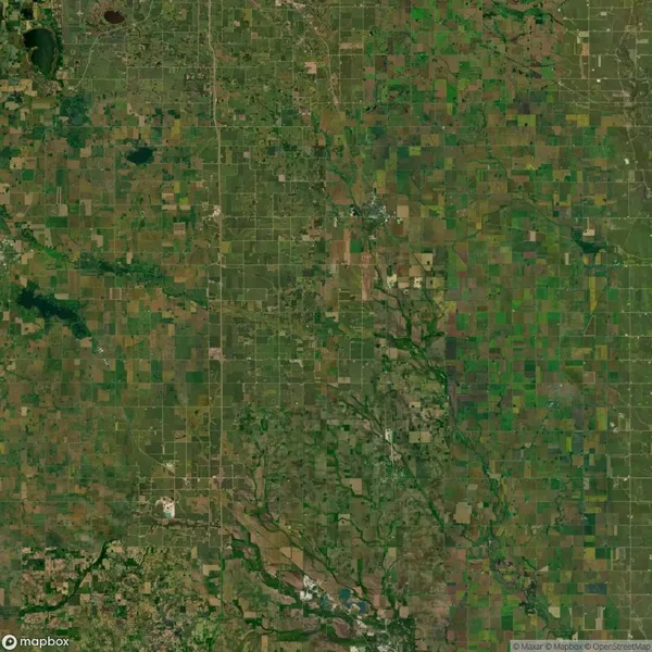 Aerial view of expansive farmland, with a patchwork of green fields and grid-like roads, interspersed with small wooded areas and streams.