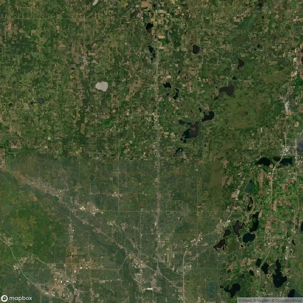 Aerial landscape view showing a patchwork of green fields, forests, and scattered lakes, with a network of roads and urban areas in lighter shades.