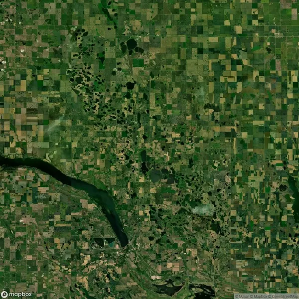 Aerial view of a vast patchwork landscape with irregular green and brown fields, scattered small ponds, and a larger body of water to the bottom left.