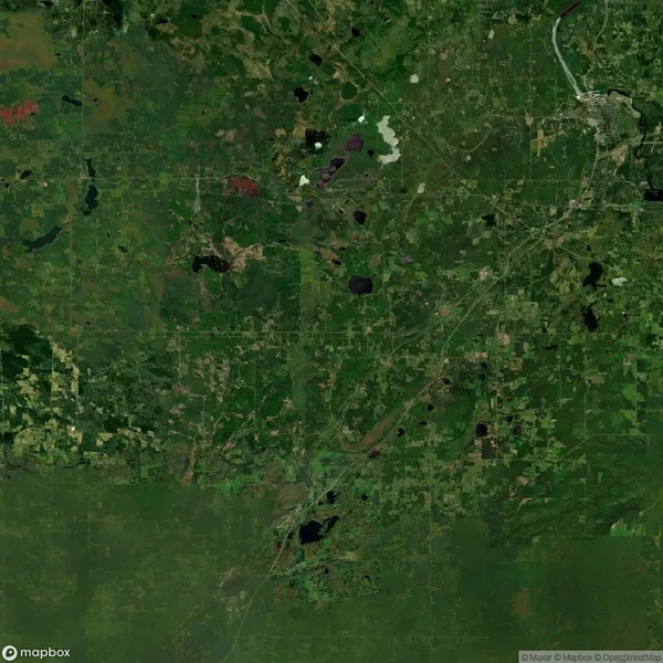 Aerial view of a vast, green landscape with scattered patches of dark and light areas, crisscrossed by roads and small bodies of water.