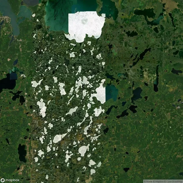 Aerial view of a forested area with scattered white patches of snow, surrounded by lakes and green vegetation.