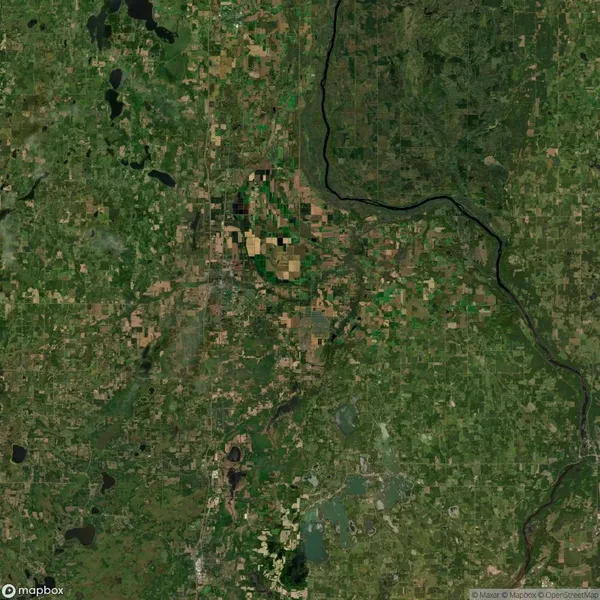 Aerial view of a green and brown patchwork landscape with fields, forests, and a winding river on the right. Small bodies of water are visible throughout the area.