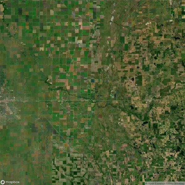 Aerial view of a patchwork of green and brown agricultural fields in a rural area, intersected by roads and small water channels.
