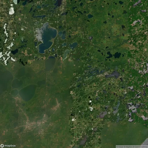 Aerial view of a landscape featuring a patchwork of agricultural fields, forested areas, small lakes, and scattered rural roads.