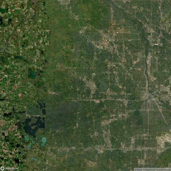 A satellite view showing a landscape with a dense grid of urban streets on the right and a more rural, green area on the left.