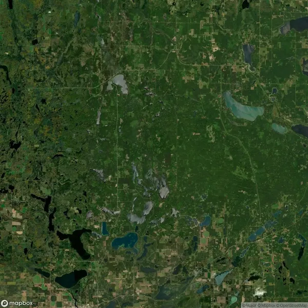 Aerial view of a green, forested landscape with scattered lakes and patches of farmland, showing a pattern of roads and natural vegetation.