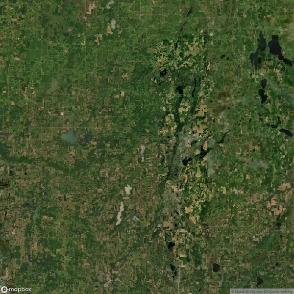 Satellite view of a mostly green landscape with patches of urban areas, roads, and water bodies visible.
