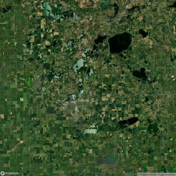 Satellite view of a landscape with a grid pattern of agricultural fields and scattered lakes and forests.