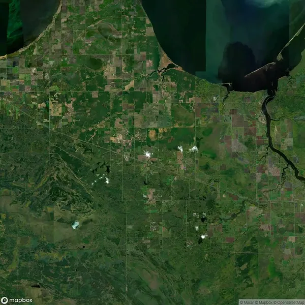 Satellite view of a landscape featuring a mix of agricultural fields, a body of water at the top, and scattered cloud coverage.