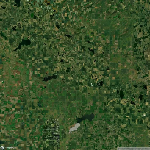 Aerial view of a rural landscape with a patchwork of green and brown fields, scattered lakes, and dense areas of forested regions.