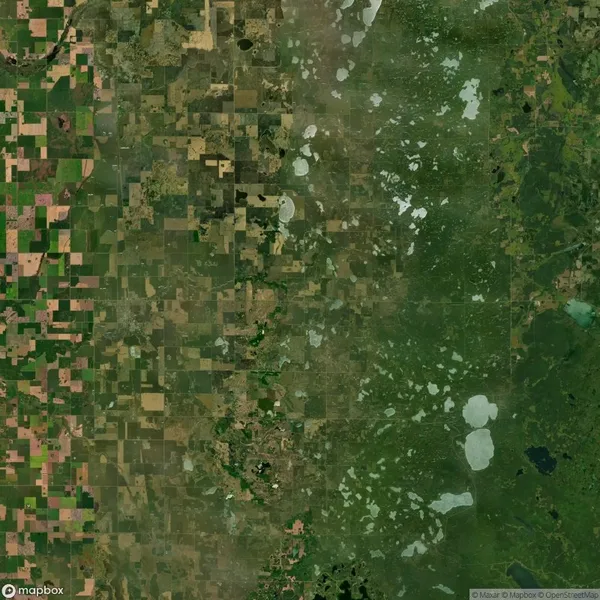 Satellite view of a landscape with a distinct divide between agricultural fields on the left and natural greenery on the right, showing patches of wetlands and varied vegetation.