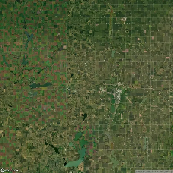 Satellite image showing a patchwork of agricultural fields, roads, and a small town in the center, with varying shades of green across the landscape.