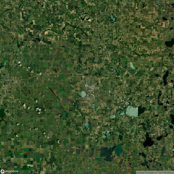 Satellite view of a rural landscape with a patchwork of green and brown fields, scattered clouds, and several lakes in different shapes across the area.
