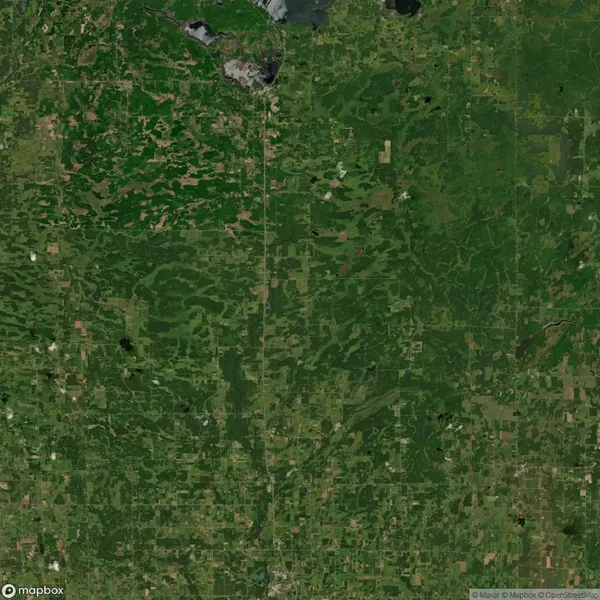 Aerial view of a landscape featuring a mix of forests, fields, and scattered bodies of water. A road is visible running vertically through the center of the image.