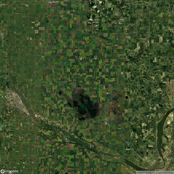 Aerial view of agricultural land with a patchwork of green and brown fields, a river running diagonally, and a large dark green area in the center.