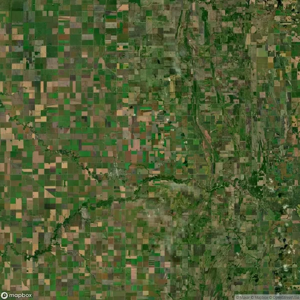 Aerial view of a patchwork landscape with rectangular agricultural fields in various shades of green and brown, intersected by winding roads and natural waterways.
