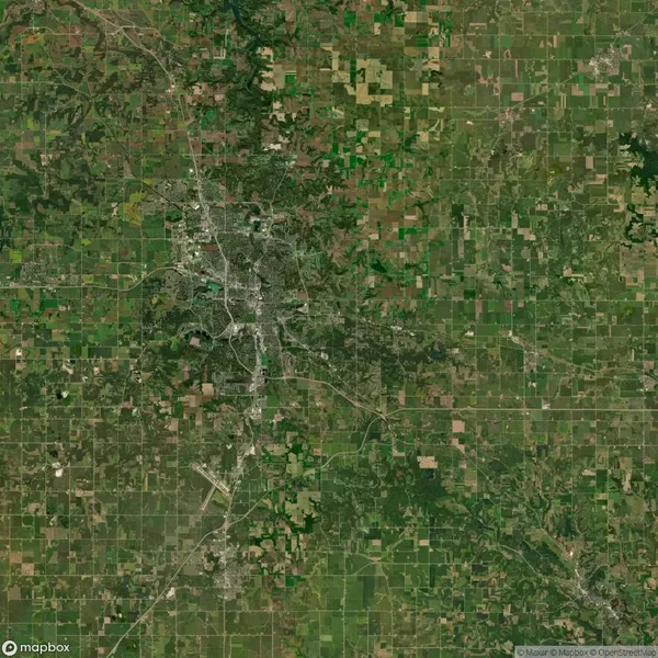 Satellite view showing a rural landscape with green and brown fields, a network of roads, and a central urban area.