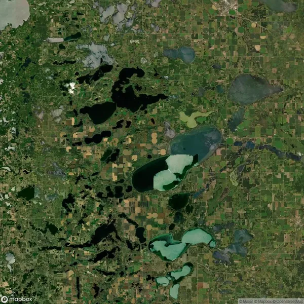 Aerial view of a landscape featuring multiple irregularly shaped lakes and green agricultural fields mixed with patches of woodlands.