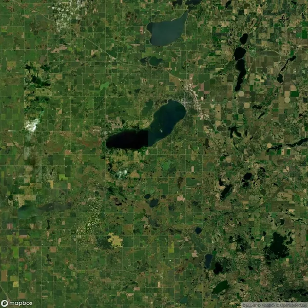 Satellite view of a landscape featuring a large lake in the center surrounded by rectangular fields and patches of greenery.