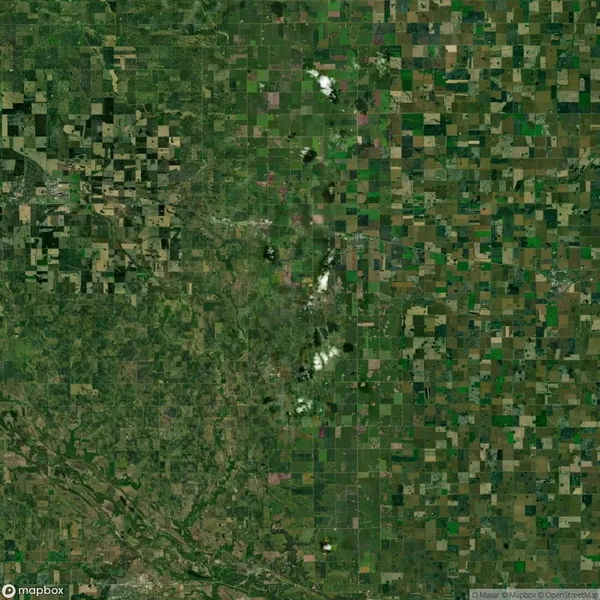 Aerial view of a large, patchwork landscape with green and brown fields, a central diagonal line of small white clouds, and a meandering river in the bottom left corner.
